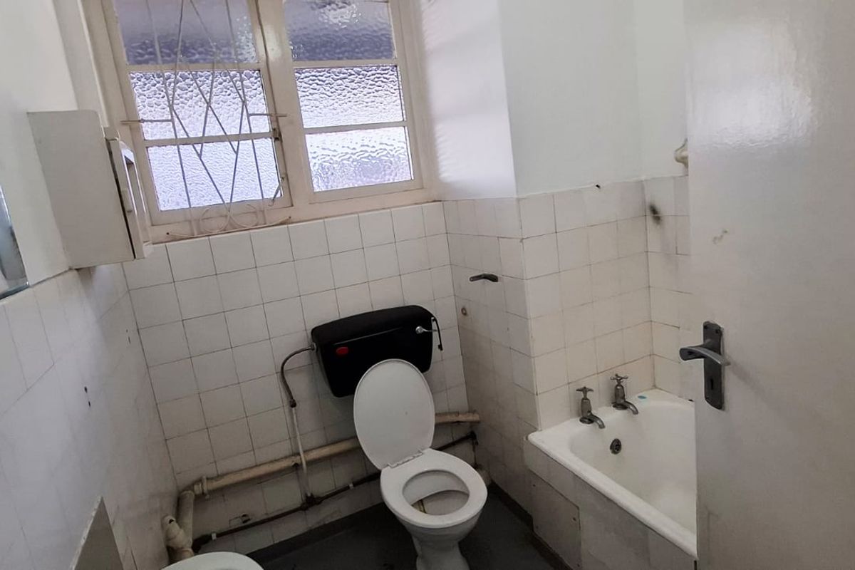 A dated bathroom featuring a bathtub, toilet, and tiled walls, requiring renovation to update the fixtures and finishes.