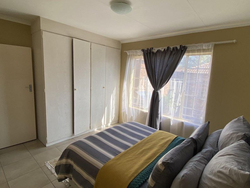 A functional bedroom featuring built-in cupboards, tiled flooring, and a window fitted with security bars, offering a practical and comfortable living space.