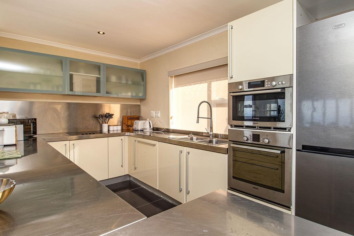Modern kitchen featuring stainless steel countertops, built-in oven and microwave, and ample cabinetry with glass-fronted upper units.