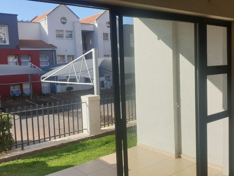 A covered patio area with tiled flooring and sliding glass doors, overlooking a residential complex parking area and garden.