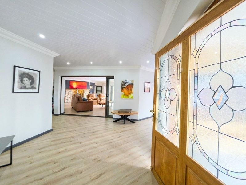 Welcoming entrance hall featuring timber laminate flooring, recessed downlighting, and a decorative stained glass timber door leading into the main living area.