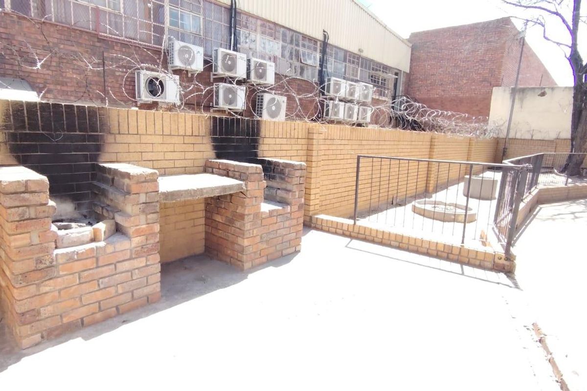 Rear outdoor area featuring a built-in brick braai, concrete paving, and a secure boundary wall with razor wire.