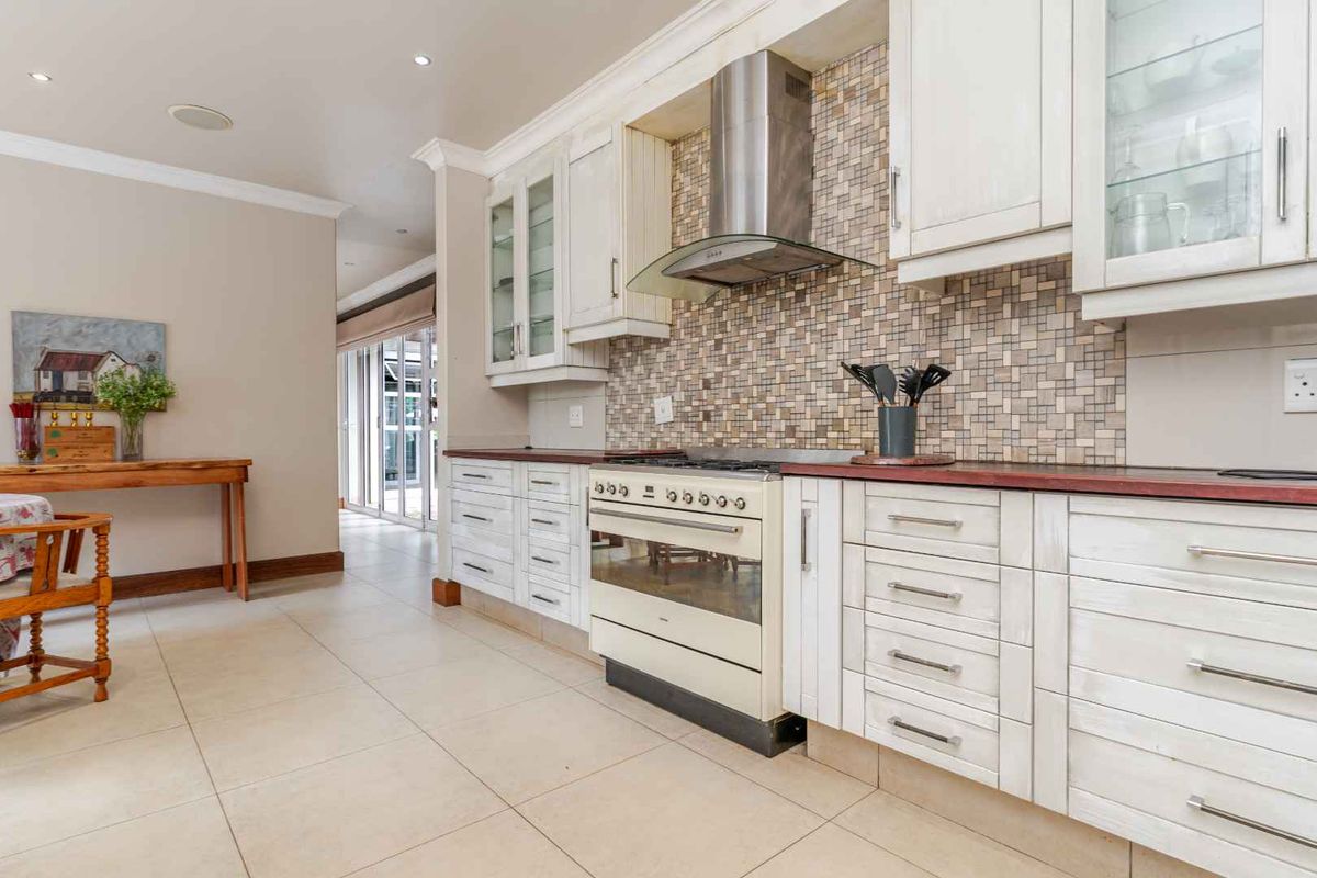 A well-maintained kitchen featuring white cabinetry, a mosaic tile backsplash, a stainless steel extractor fan, and a freestanding oven.