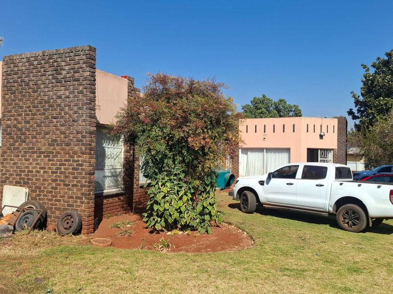 Front view of a single-story brick house featuring security bars on windows and a large front garden area.