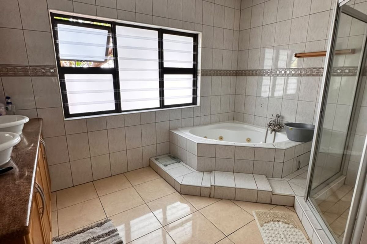 Spacious bathroom featuring a corner jetted bathtub, separate shower enclosure, double vanity, and neutral floor-to-ceiling tiling.