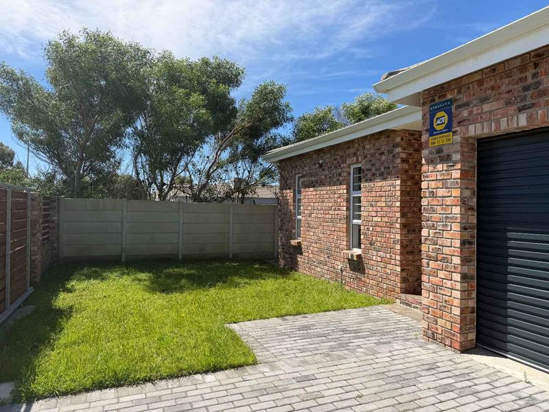 A well-maintained rear exterior view featuring a face brick facade, paved patio area, and a private garden enclosed by a precast concrete boundary wall.