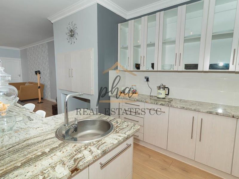 Modern kitchen featuring granite countertops, ample built-in cabinetry with glass-front uppers, undermount sink, and light laminate flooring.