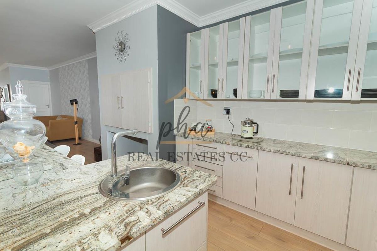 Modern kitchen featuring granite countertops, ample built-in cabinetry with glass-front uppers, undermount sink, and light laminate flooring.