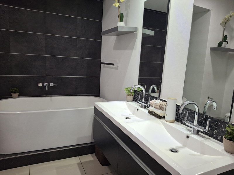 Modern bathroom featuring a sleek double vanity with integrated sinks, wall-mounted faucets, and a contemporary freestanding bathtub against a dark tiled feature wall.