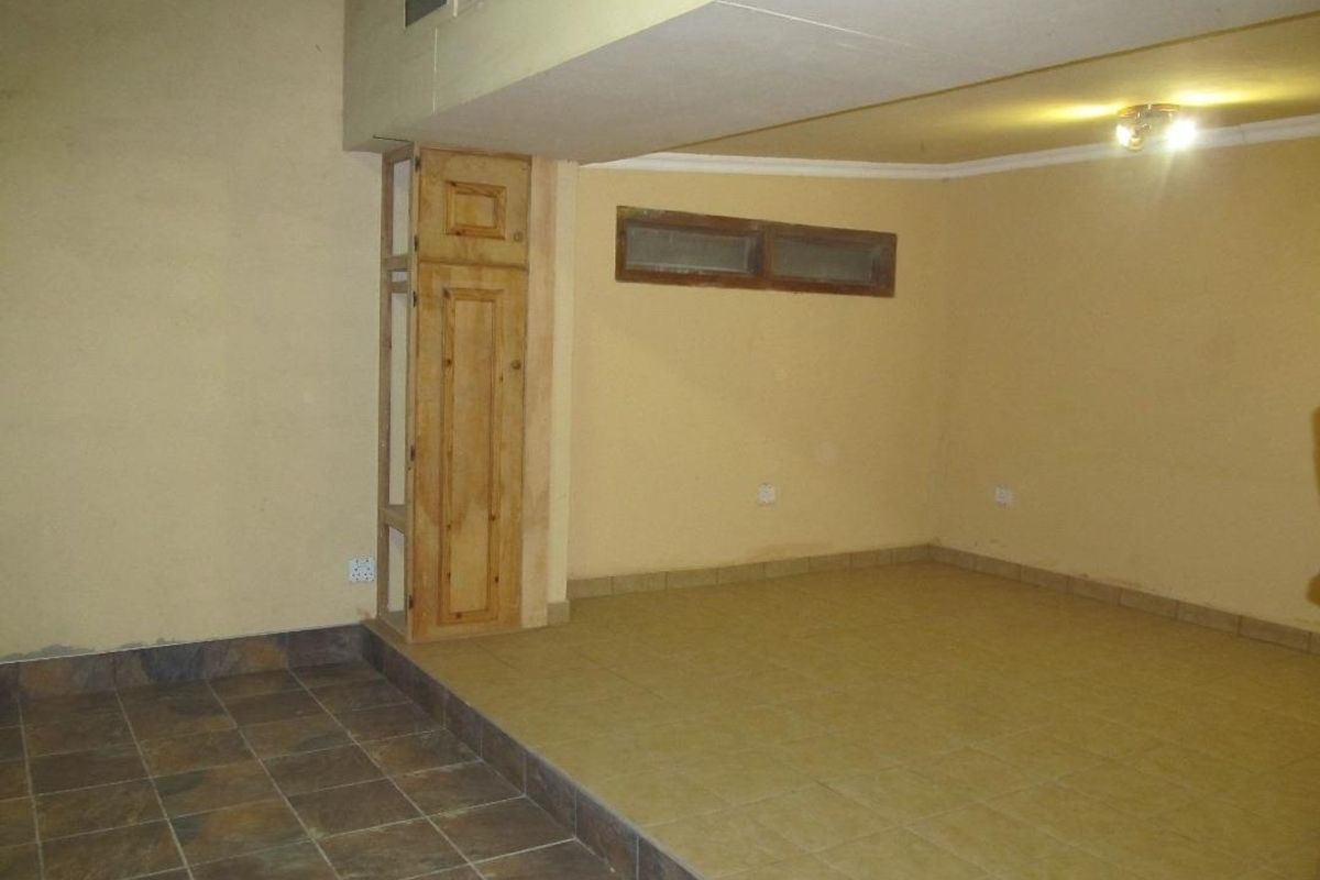 An empty, multi-level interior space featuring tiled flooring, a built-in wooden cabinet, and a raised platform area.