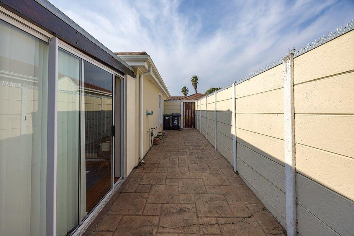 A narrow paved side passage featuring a sliding glass door entrance, enclosed by a precast concrete boundary wall with security spikes.