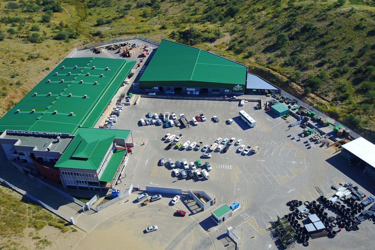 Aerial view of a large commercial retail facility featuring extensive warehouse space, a paved parking lot, and secure perimeter fencing.