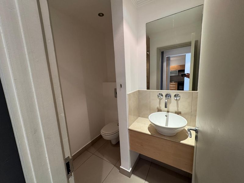 A modern, compact bathroom featuring a floating vanity with a vessel sink, wall-mounted faucet, and a separate enclosed toilet area.
