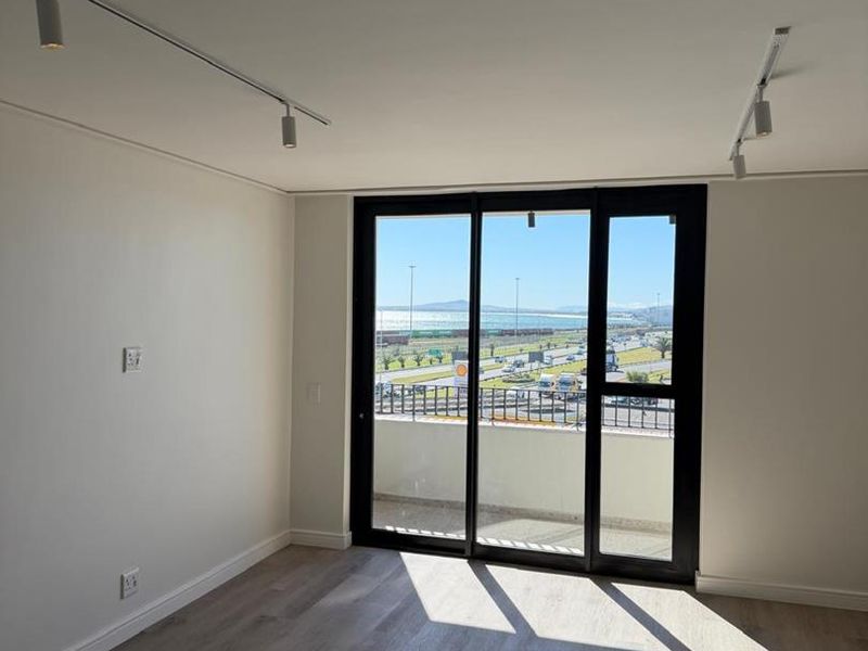 Bright and modern empty living area featuring laminate flooring, track lighting, and large sliding glass doors opening to a balcony with coastal views.