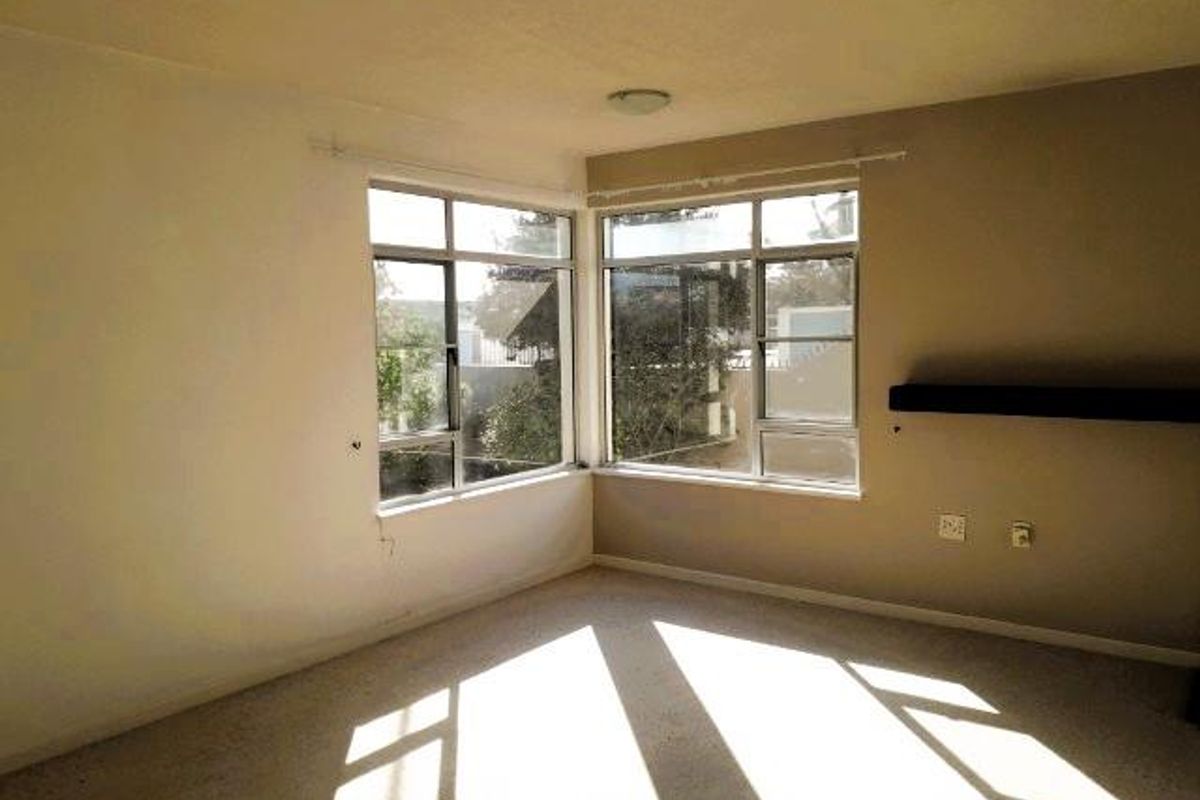 A bright, empty bedroom featuring large corner windows that provide ample natural light and a neutral color palette.
