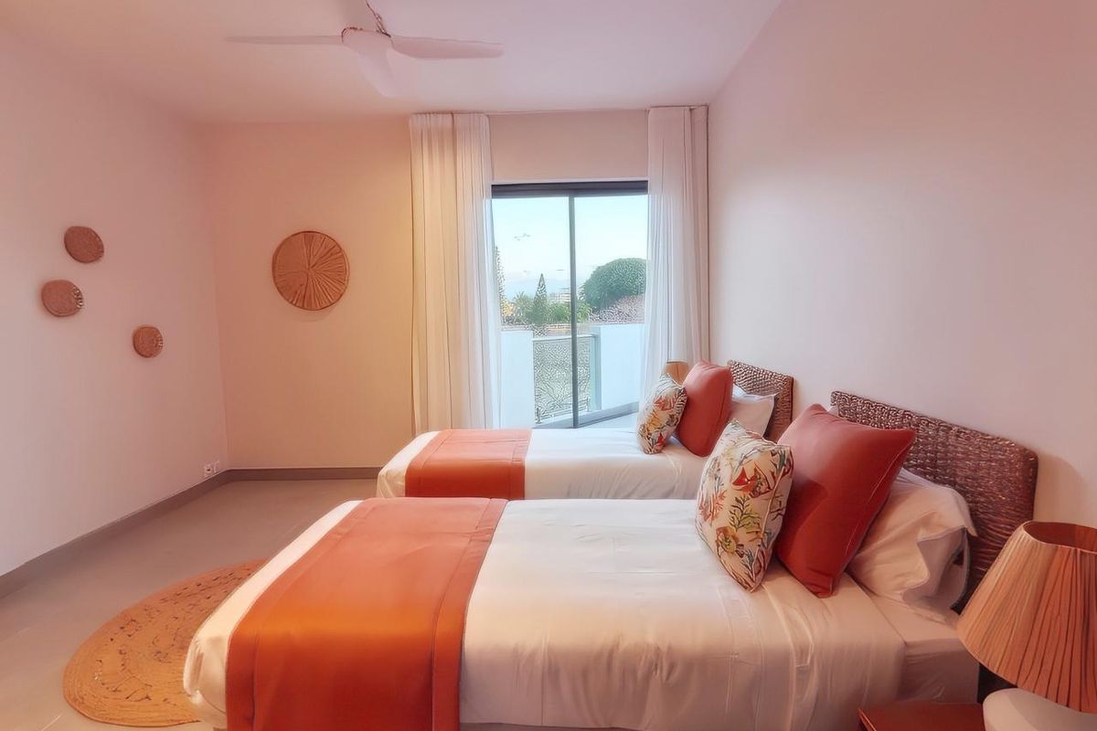 A bright and airy bedroom featuring a ceiling fan, neutral flooring, and sliding glass doors that open onto a private balcony.
