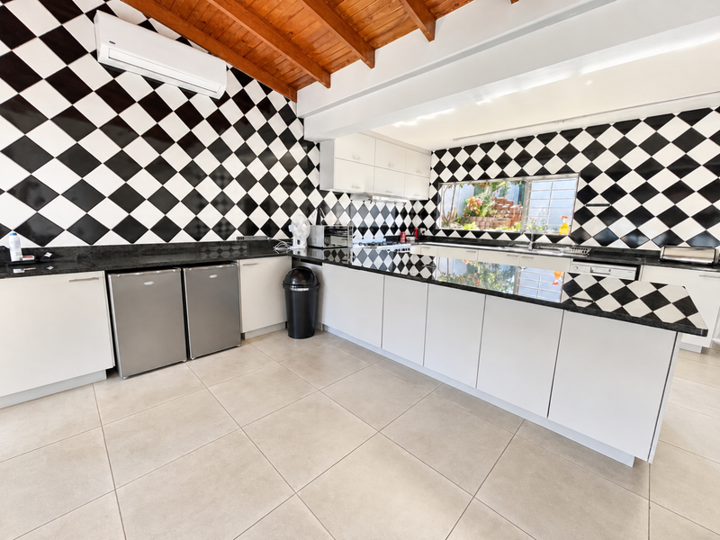 Spacious kitchen featuring a bold black and white checkered backsplash, granite countertops, ample cabinetry, and exposed timber ceiling beams.