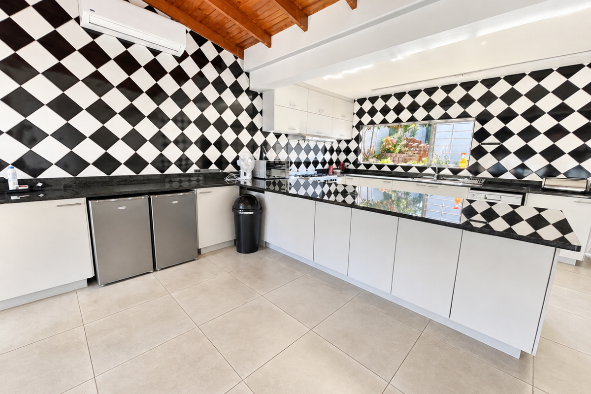 Spacious kitchen featuring a bold black and white checkered backsplash, granite countertops, ample cabinetry, and exposed timber ceiling beams.