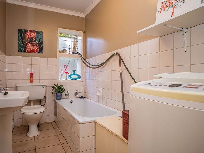 A functional bathroom featuring a pedestal basin, toilet, and built-in bathtub with tiled finishes, requiring some cosmetic updates to modernize the space.