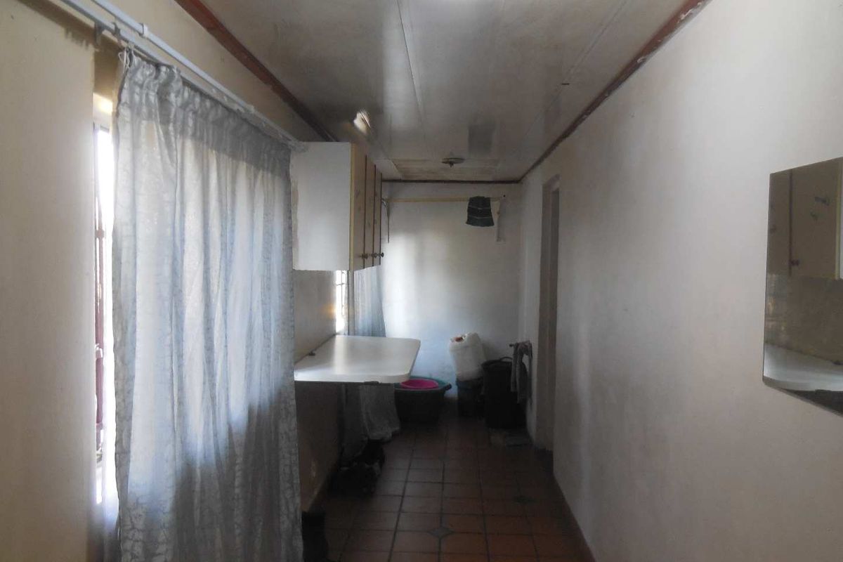 A narrow kitchen area featuring tiled flooring, wall-mounted cabinetry, and a fixed counter, requiring cosmetic updates to improve its overall condition.