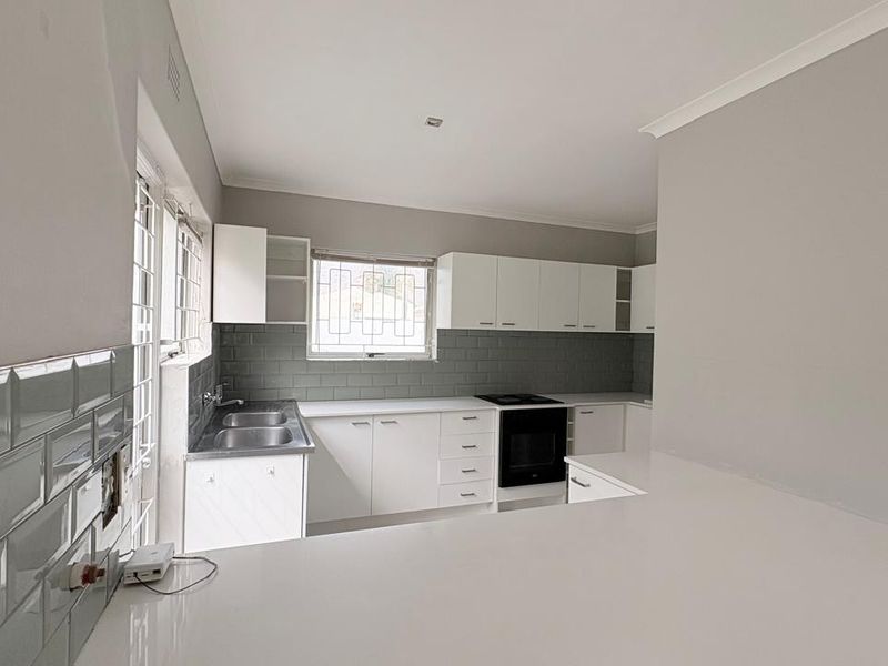 A clean, modern kitchen featuring white cabinetry, subway tile backsplash, stainless steel sink, and built-in oven with ample quartz countertop workspace.