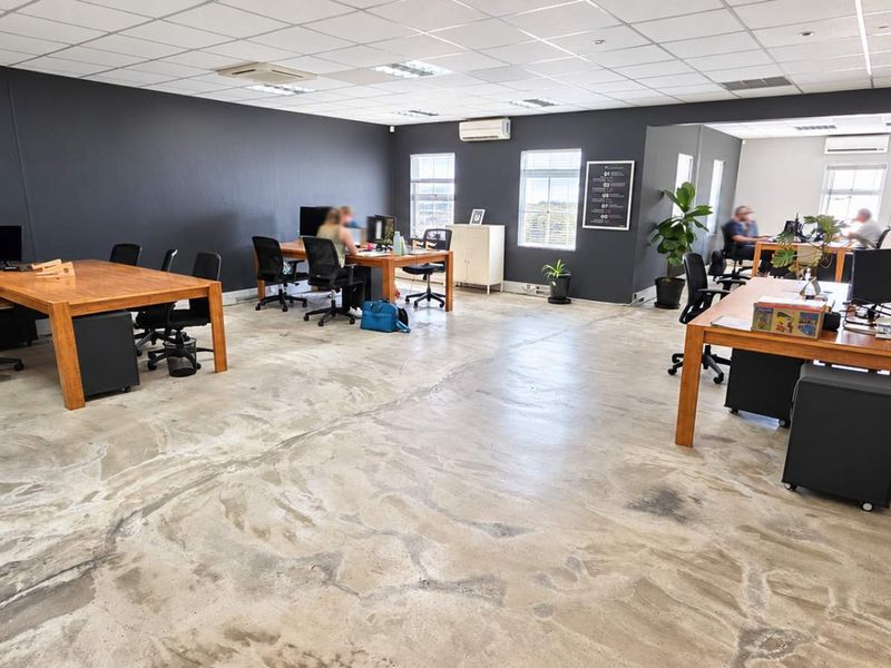 Spacious open-plan office area featuring polished concrete floors, a suspended ceiling with recessed lighting, and integrated air conditioning units.