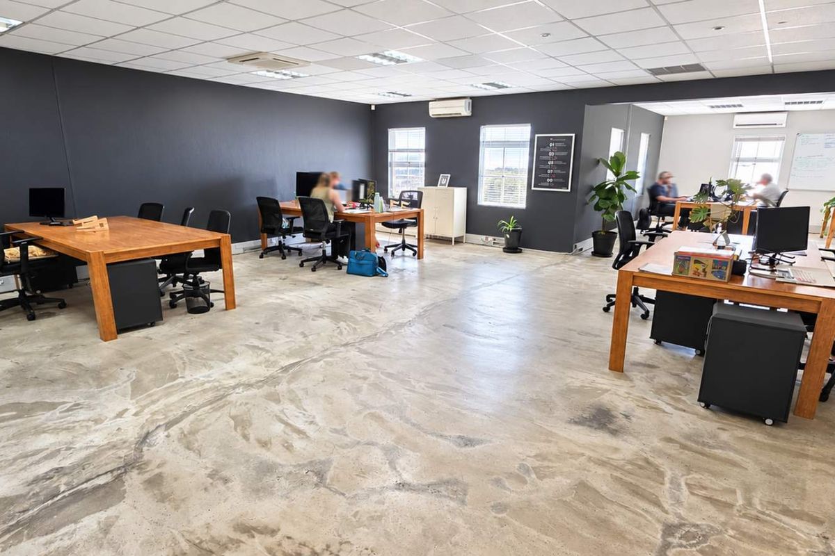 Spacious open-plan office area featuring polished concrete floors, a suspended ceiling with recessed lighting, and integrated air conditioning units.