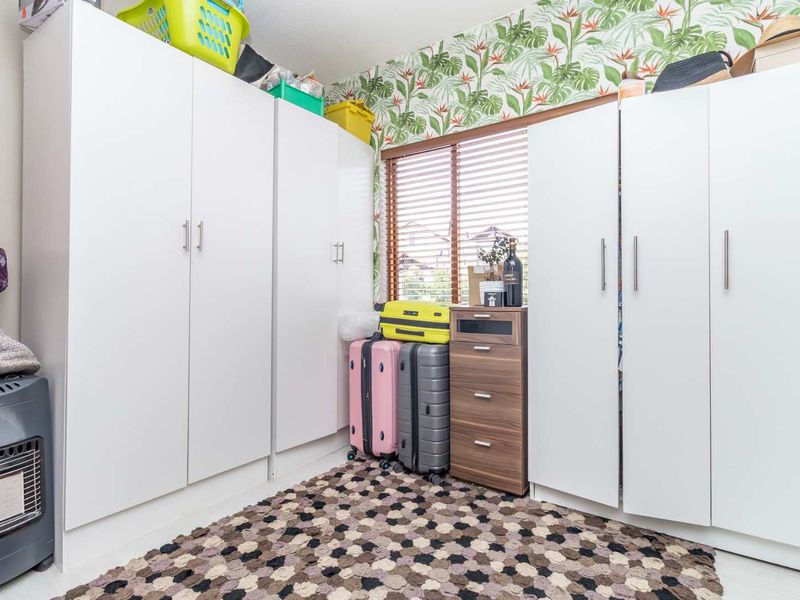 A bedroom featuring extensive built-in white cabinetry for storage, a window with wooden blinds, and decorative wallpaper.