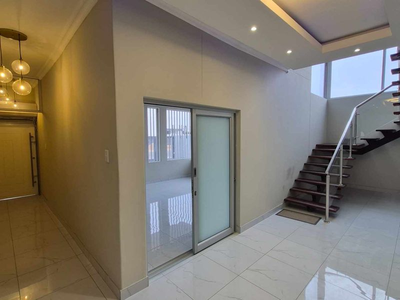 Modern entrance hall featuring a striking floating staircase with glass balustrade, sleek tiled flooring, and contemporary recessed ceiling lighting.