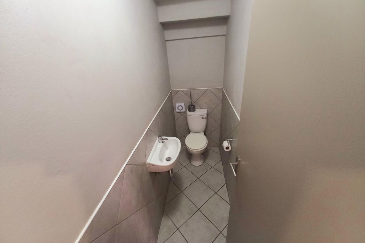 A compact guest cloakroom featuring a wall-mounted basin and a standard toilet with tiled flooring and partial wall tiling.