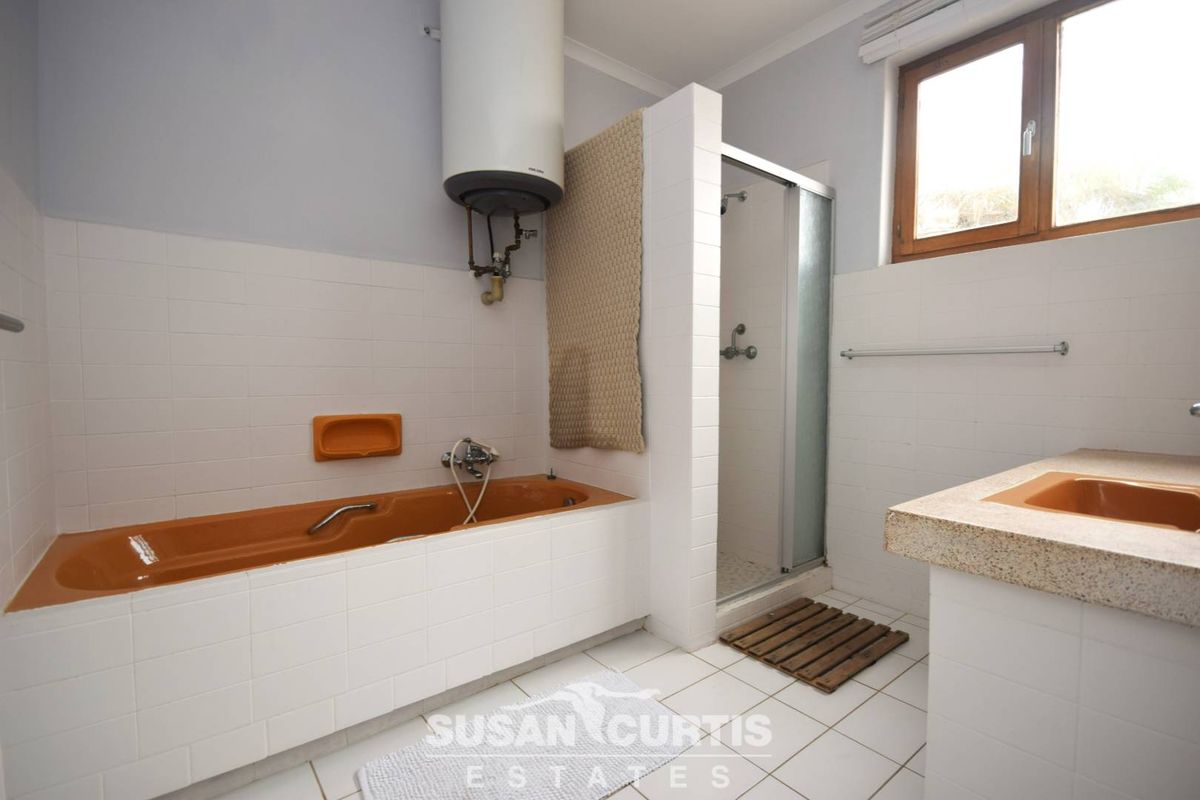 A dated bathroom featuring a built-in orange bathtub, separate shower enclosure, and a stone-topped vanity with an integrated orange basin.