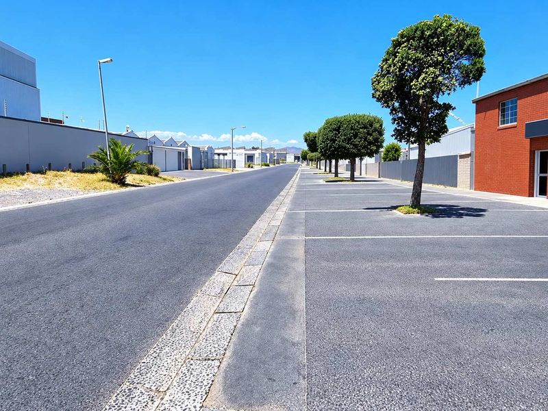 A clear street view of an industrial park featuring paved parking bays, well-maintained asphalt roads, and secure perimeter fencing.