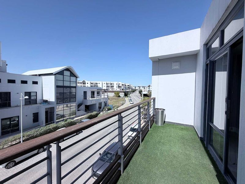 A modern balcony featuring artificial grass flooring, a metal safety railing, and direct access to the interior through a large sliding glass door.