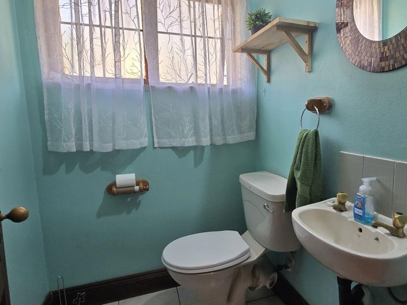 A functional bathroom featuring a wall-mounted basin, toilet, and window with security bars, finished with light blue walls.