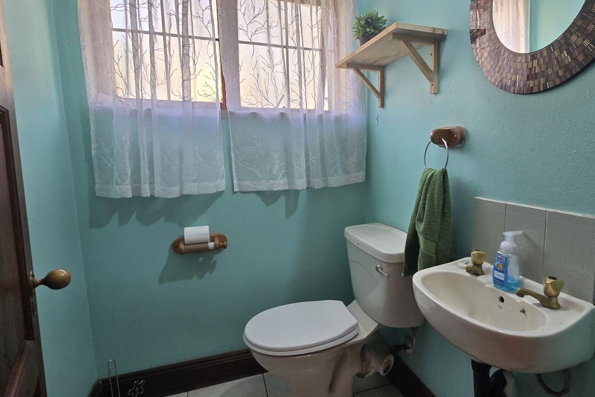 A functional bathroom featuring a wall-mounted basin, toilet, and window with security bars, finished with light blue walls.