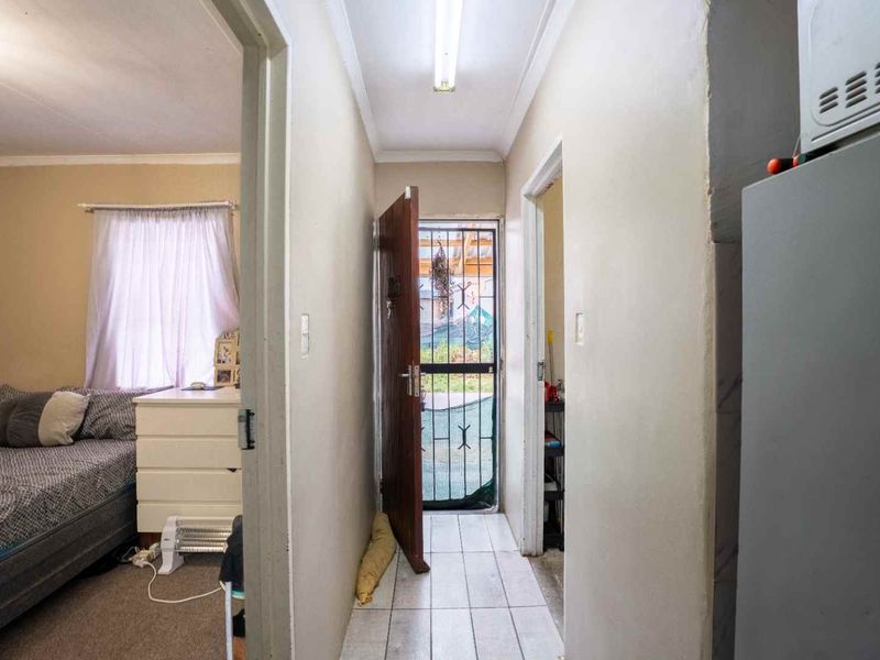 A functional hallway featuring tiled flooring and a security gate leading to the exterior, connecting to adjacent rooms.