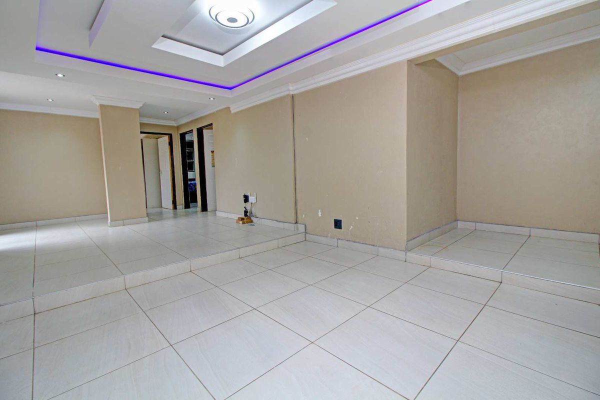 An empty, open-plan living area featuring a raised floor platform, recessed ceiling with integrated LED lighting, and neutral tiled flooring throughout.