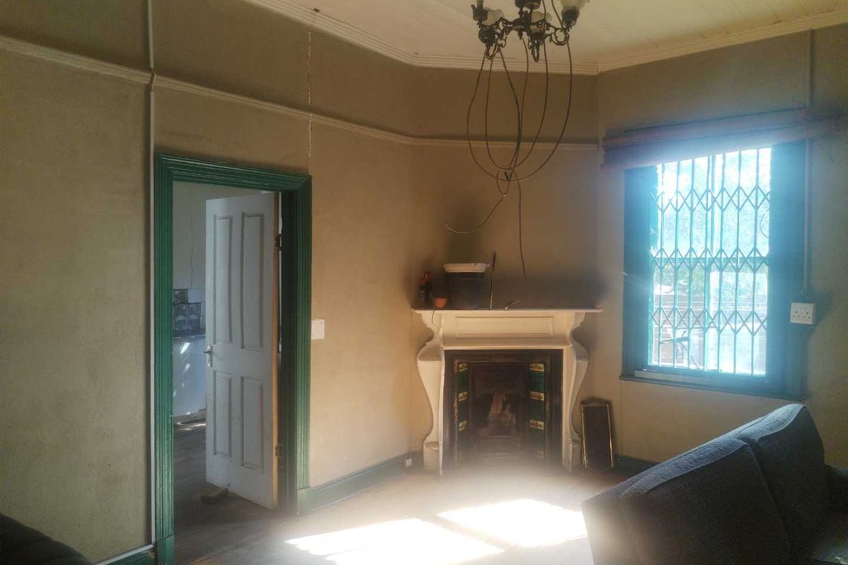 A living room featuring a traditional fireplace, timber flooring, and period-style door frames, requiring cosmetic updates to restore its character.