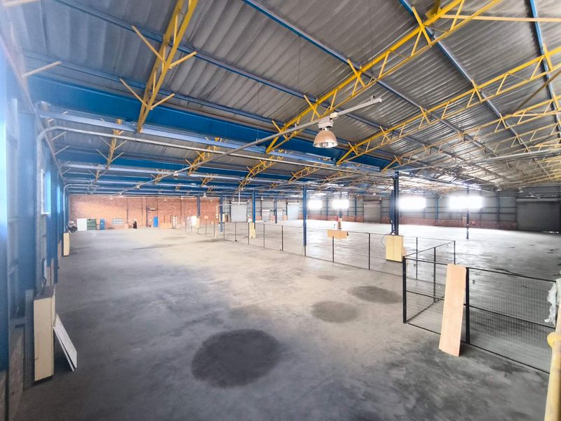 Expansive industrial warehouse space featuring high exposed steel trusses, concrete flooring, and partitioned areas, suitable for manufacturing or storage operations.