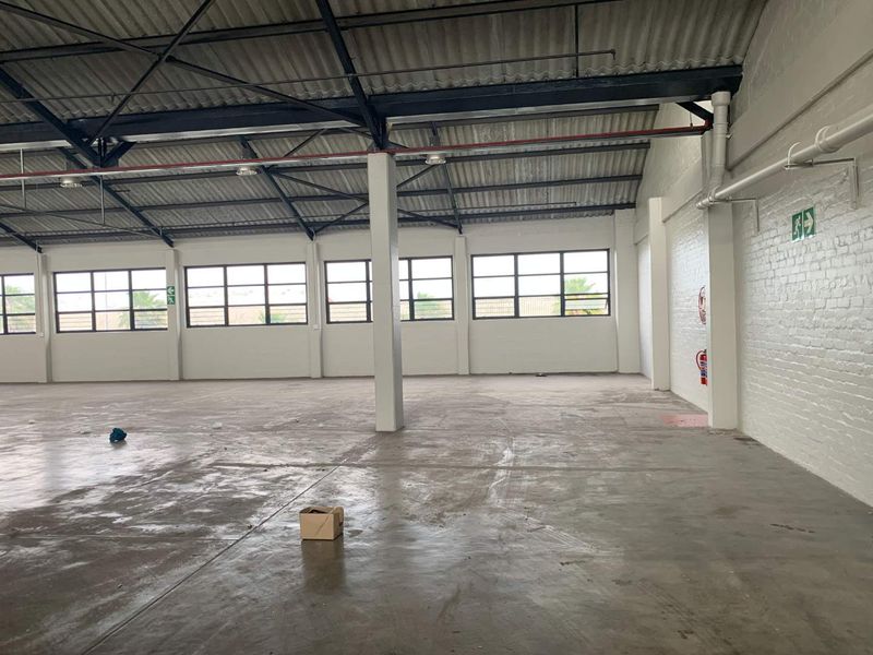Spacious industrial warehouse unit featuring high exposed steel trusses, large steel-framed windows, painted brick walls, and durable concrete flooring.
