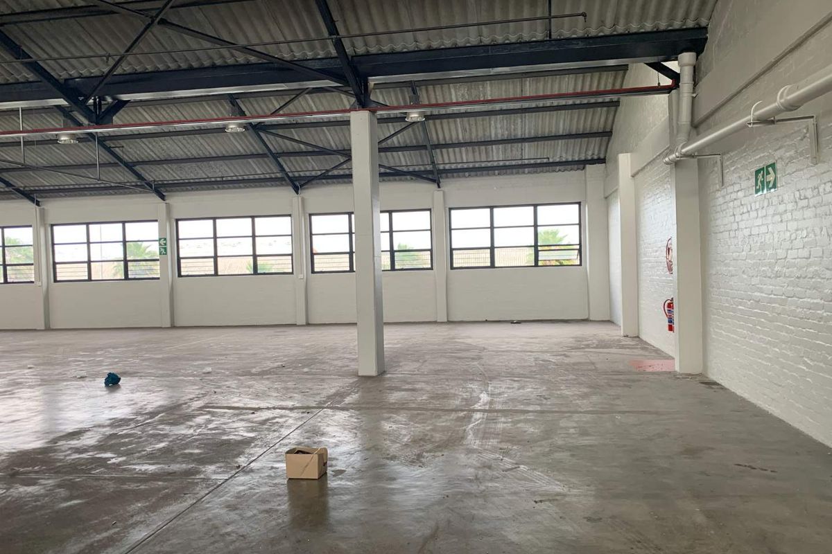 Spacious industrial warehouse unit featuring high exposed steel trusses, large steel-framed windows, painted brick walls, and durable concrete flooring.