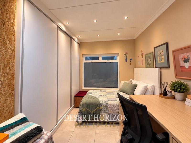 A well-lit bedroom featuring built-in sliding door wardrobes, tiled flooring, and recessed ceiling lighting.