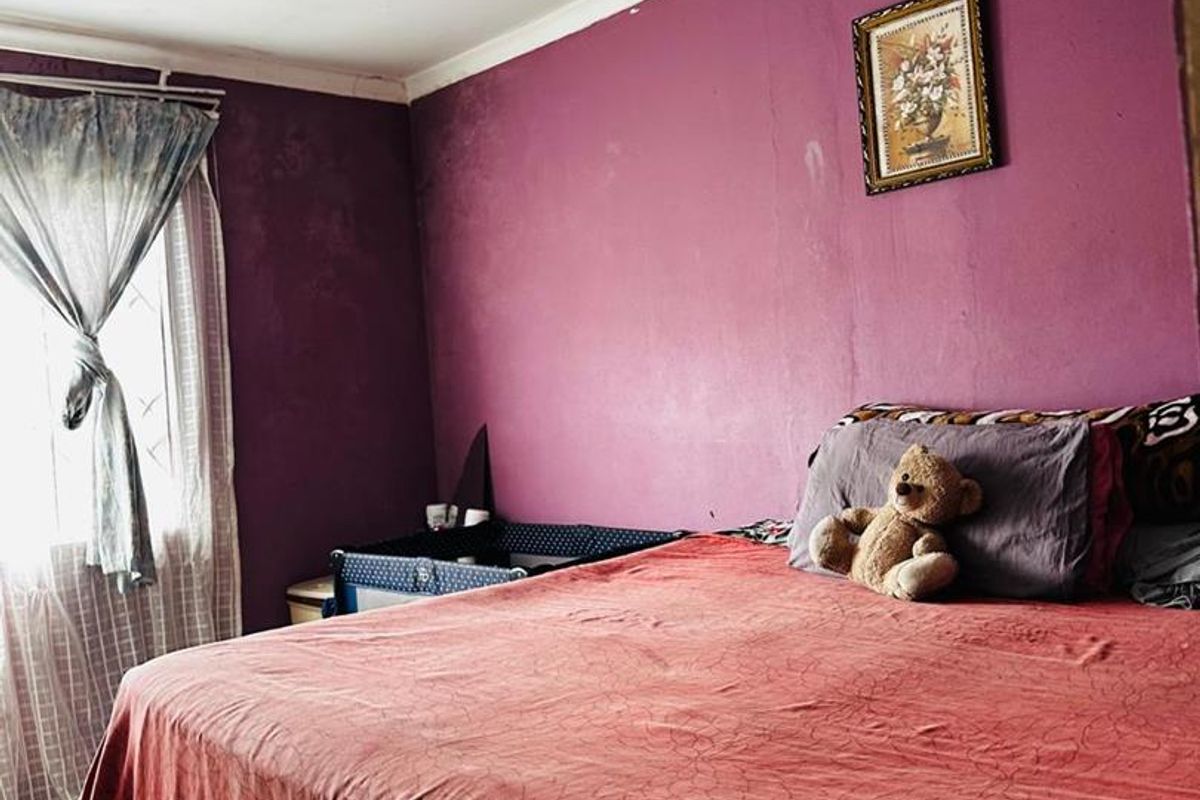 A bedroom featuring tiled flooring and purple painted walls, with visible signs of wear on the ceiling and wall surfaces.