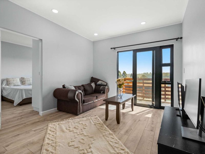 A bright living room featuring modern laminate flooring, recessed downlights, and a sliding glass door providing access to an outdoor balcony area.