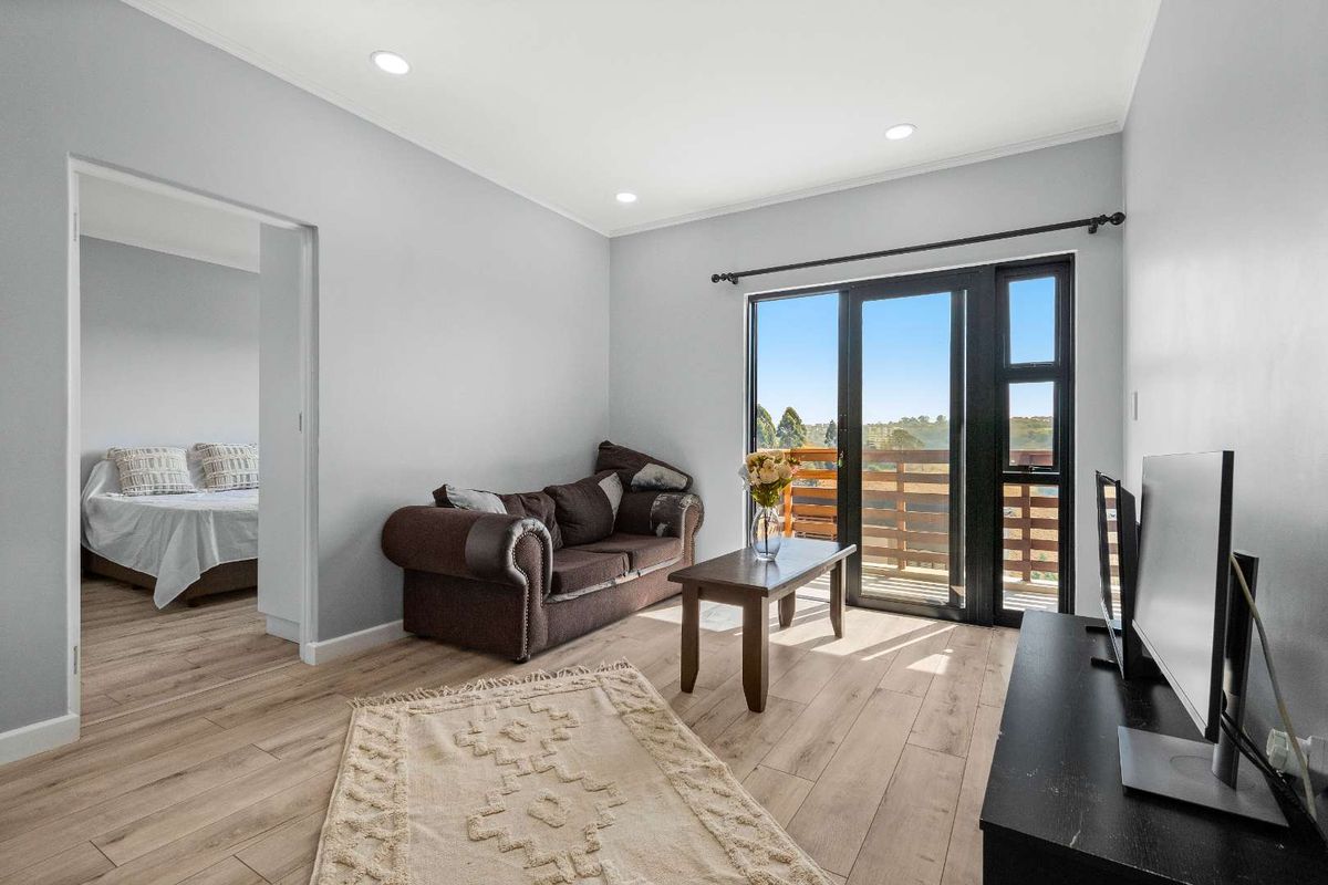 A bright living room featuring modern laminate flooring, recessed downlights, and a sliding glass door providing access to an outdoor balcony area.