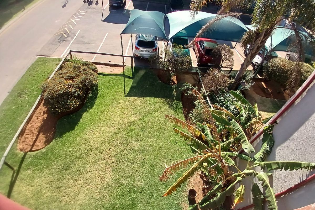 An elevated view of the apartment complex grounds, featuring a well-maintained lawn, landscaped garden beds, and covered parking bays.