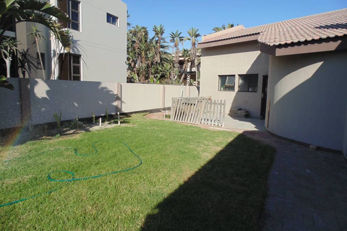 A private rear garden area featuring a lawn, paved walkway, and perimeter boundary wall, providing a functional outdoor space for the property.