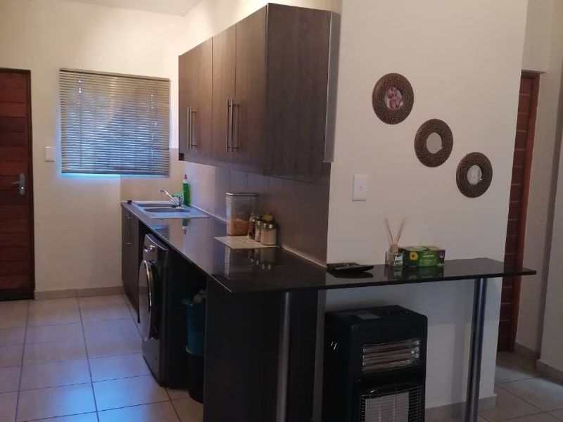 A functional kitchen area featuring dark wood cabinetry, granite countertops, a stainless steel sink, and neutral tiled flooring.