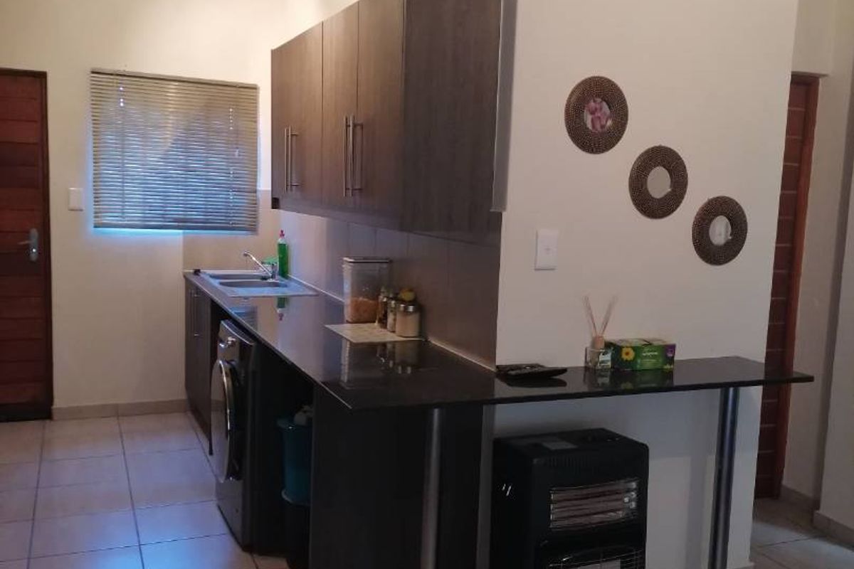 A functional kitchen area featuring dark wood cabinetry, granite countertops, a stainless steel sink, and neutral tiled flooring.