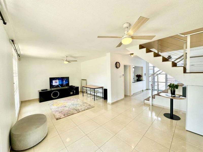 Spacious open-plan living area featuring tiled flooring, ceiling fans, and a modern staircase with stainless steel balustrades, offering a bright and functional layout.